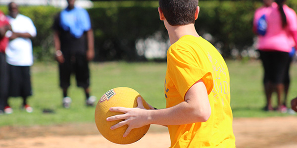 Person holding a kickball in a field.